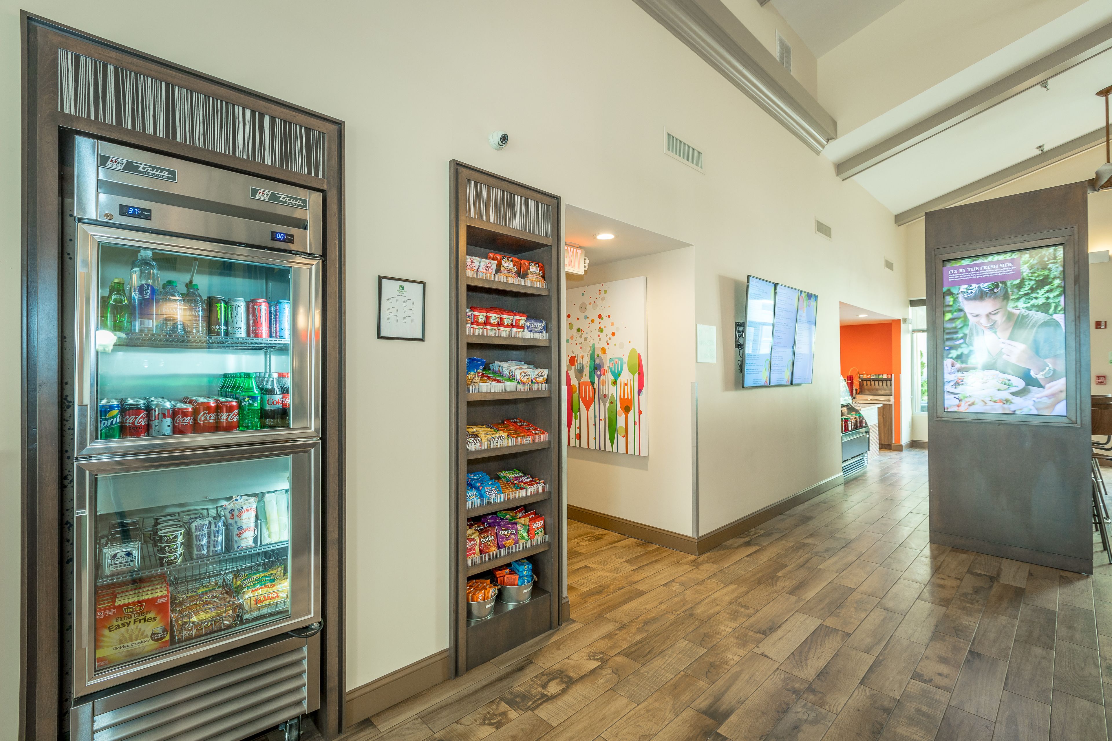 A hallway with a refrigerated beverage dispenser, a snack vending machine, and a digital menu board.