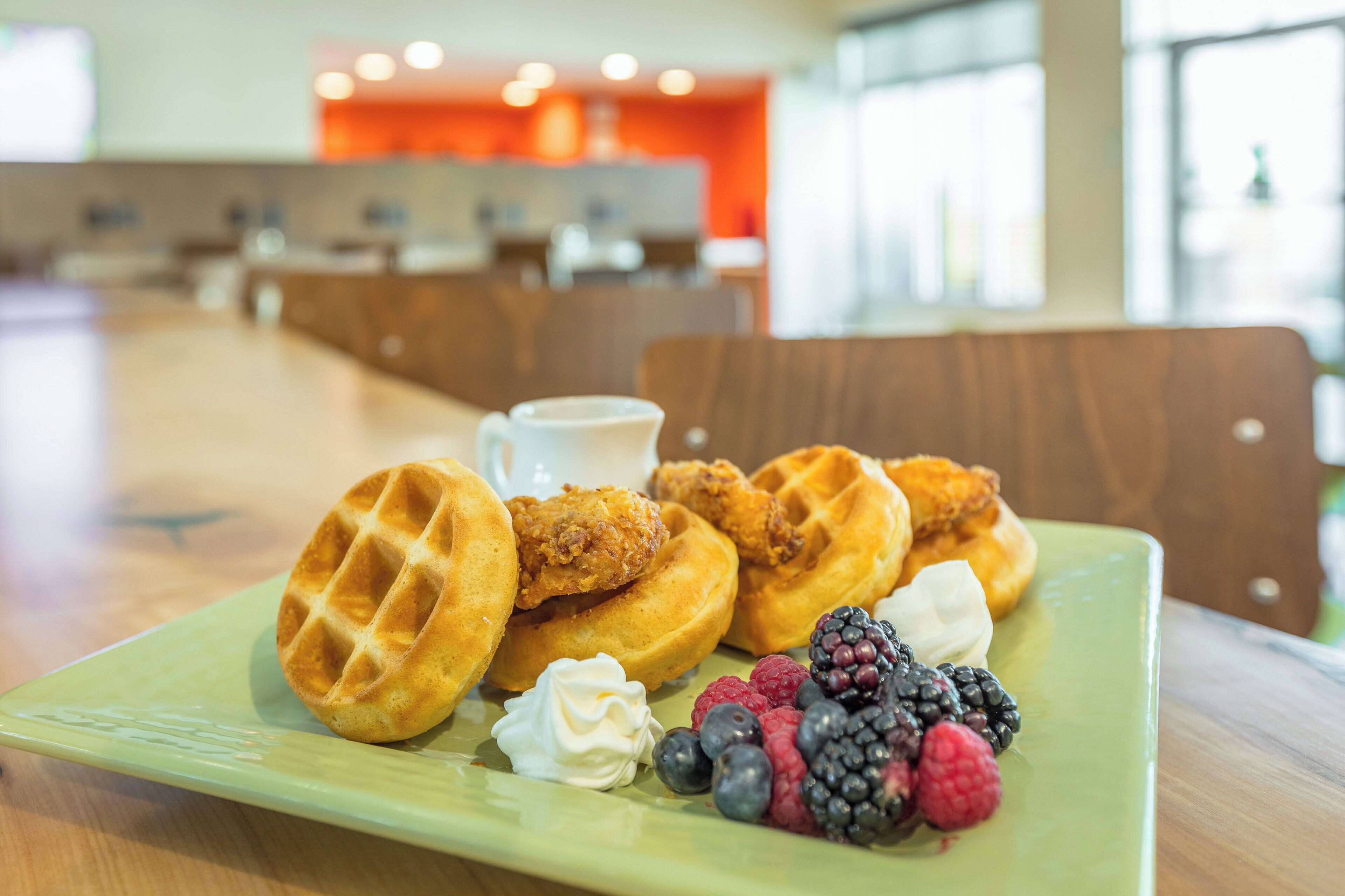 Une assiette de gaufres accompagnée de poulet frit et de fruits rouges, une tasse de café et une chaise en bois.