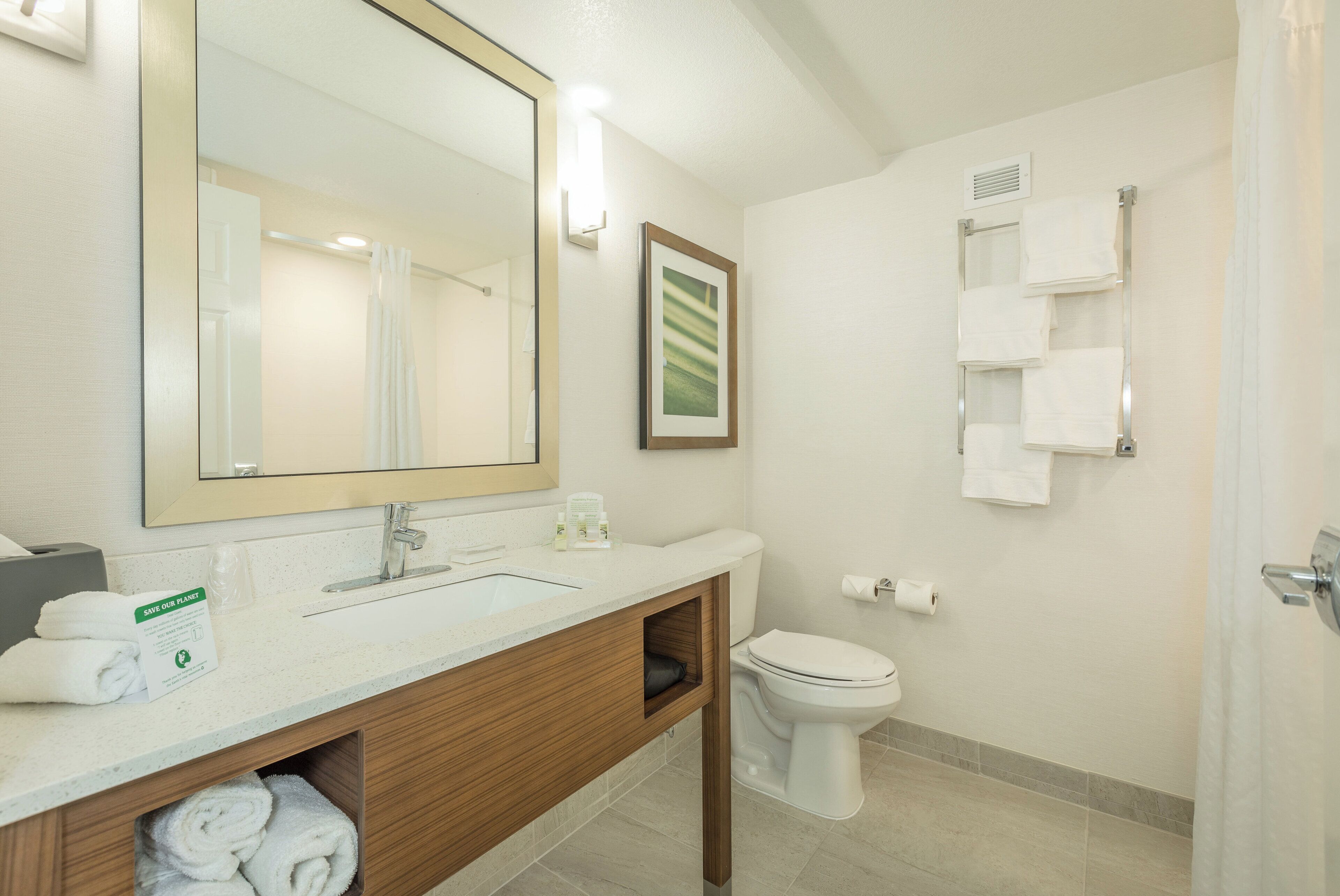 A bathroom with a large mirror, a sink, a toilet, and a towel rack.