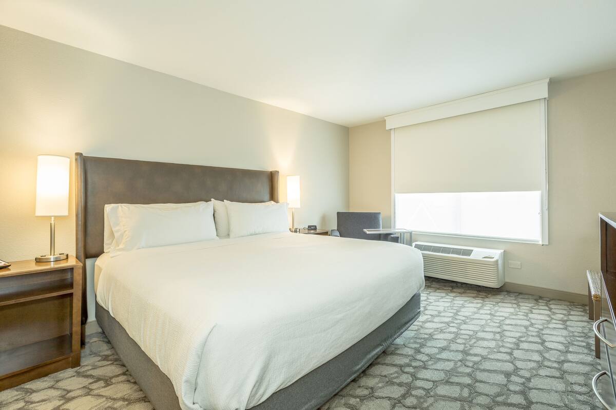 Une chambre d’hôtel avec un grand lit, des lampes de chevet, un bureau et une fenêtre avec des stores.