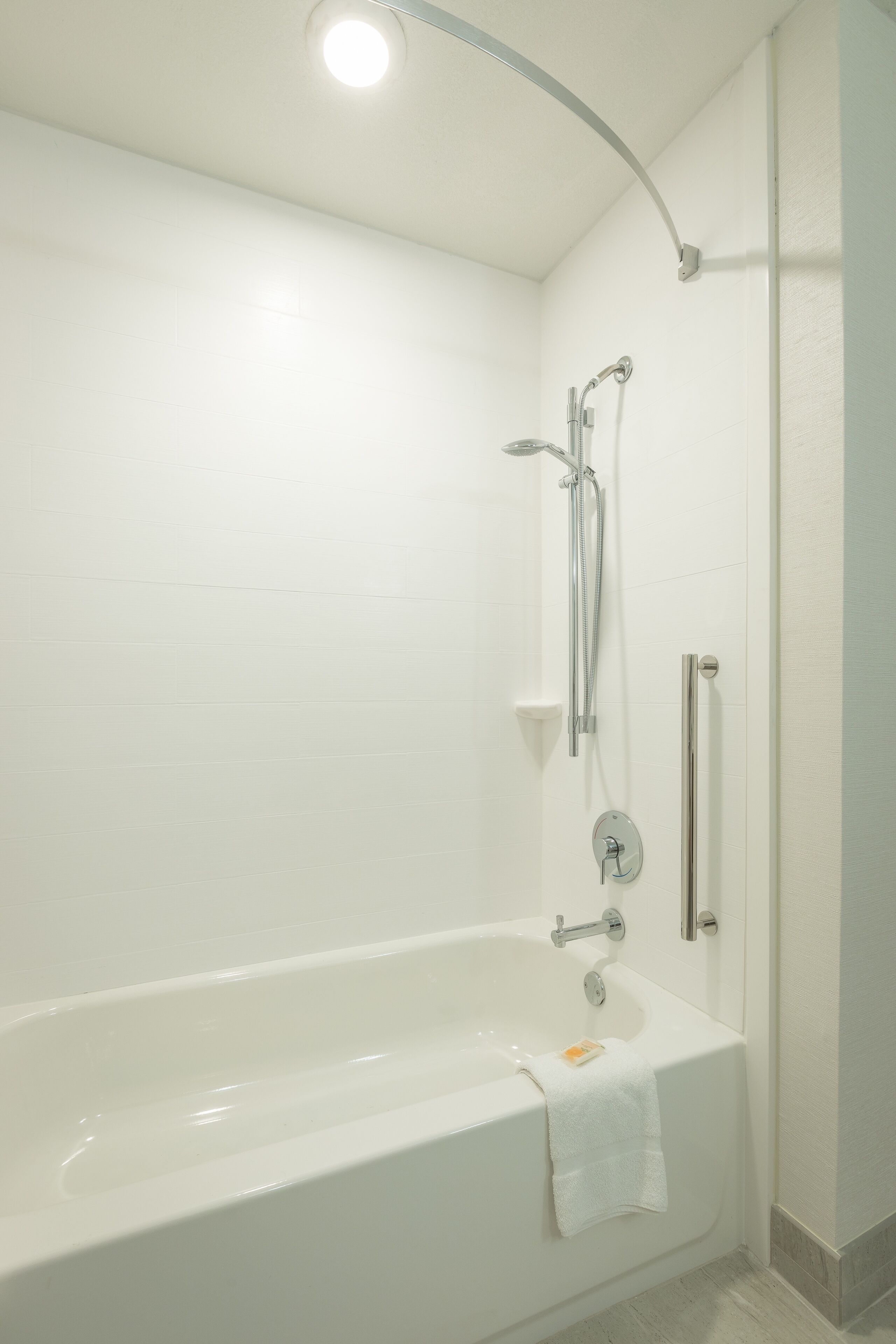 A modern bathroom with a white bathtub, a showerhead, and a handrail.