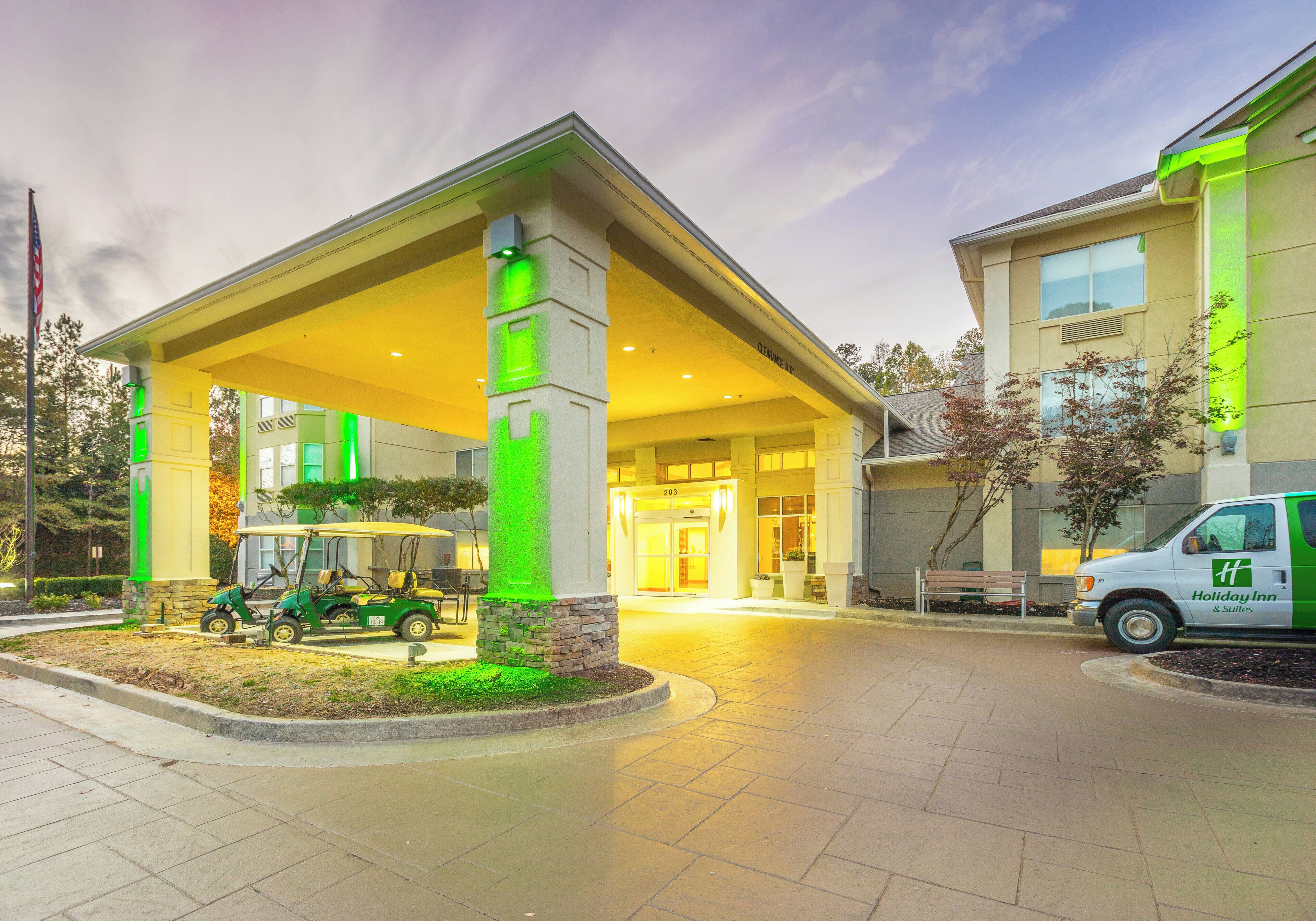 A hotel entrance with a covered waiting area, a golf cart, and a Holiday Inn & Suites sign.
