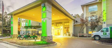 A hotel entrance with a covered waiting area, a golf cart, and a Holiday Inn & Suites sign.