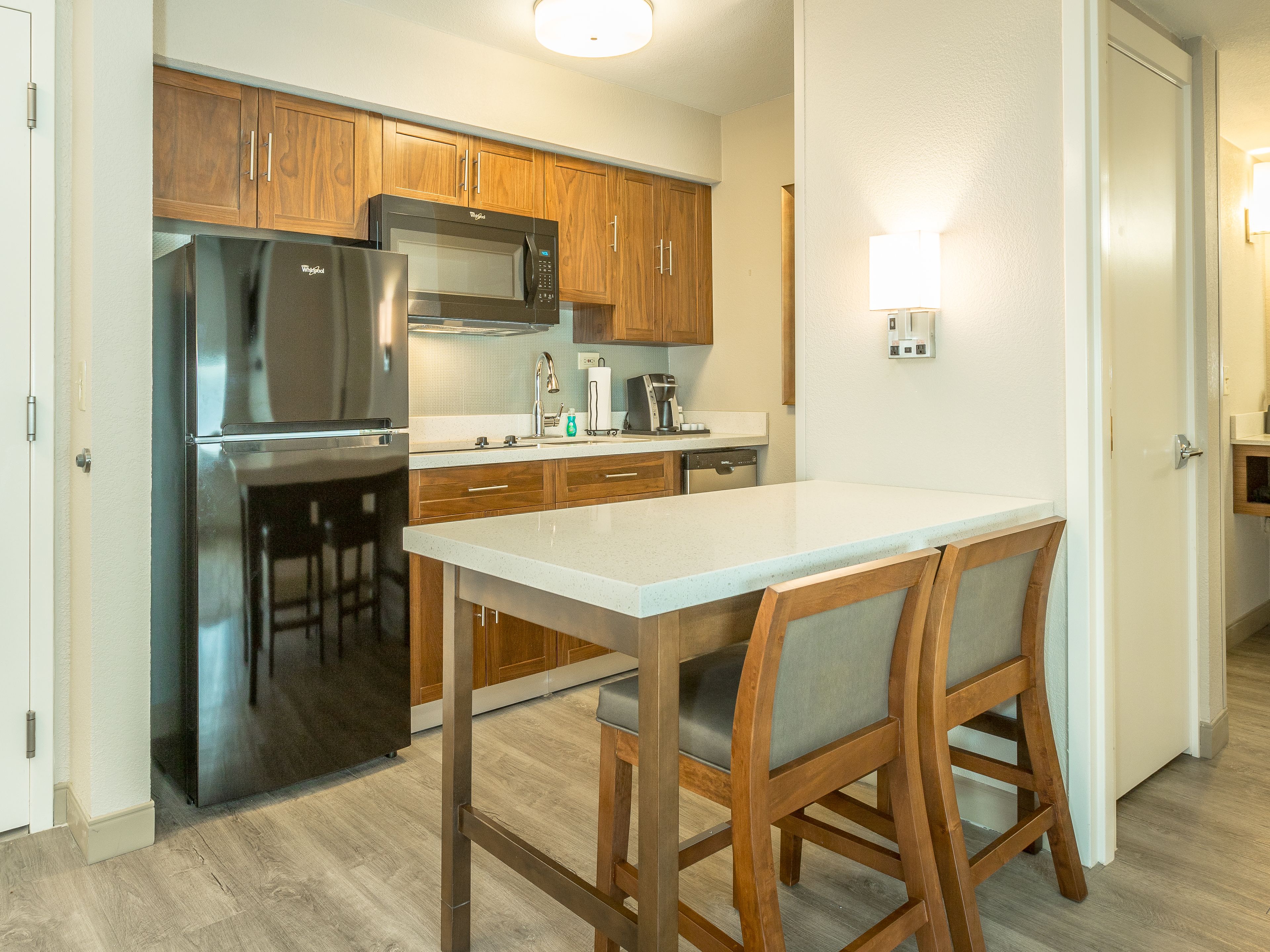 A modern kitchen with wooden cabinets, stainless steel appliances, a white countertop, and two wooden chairs.