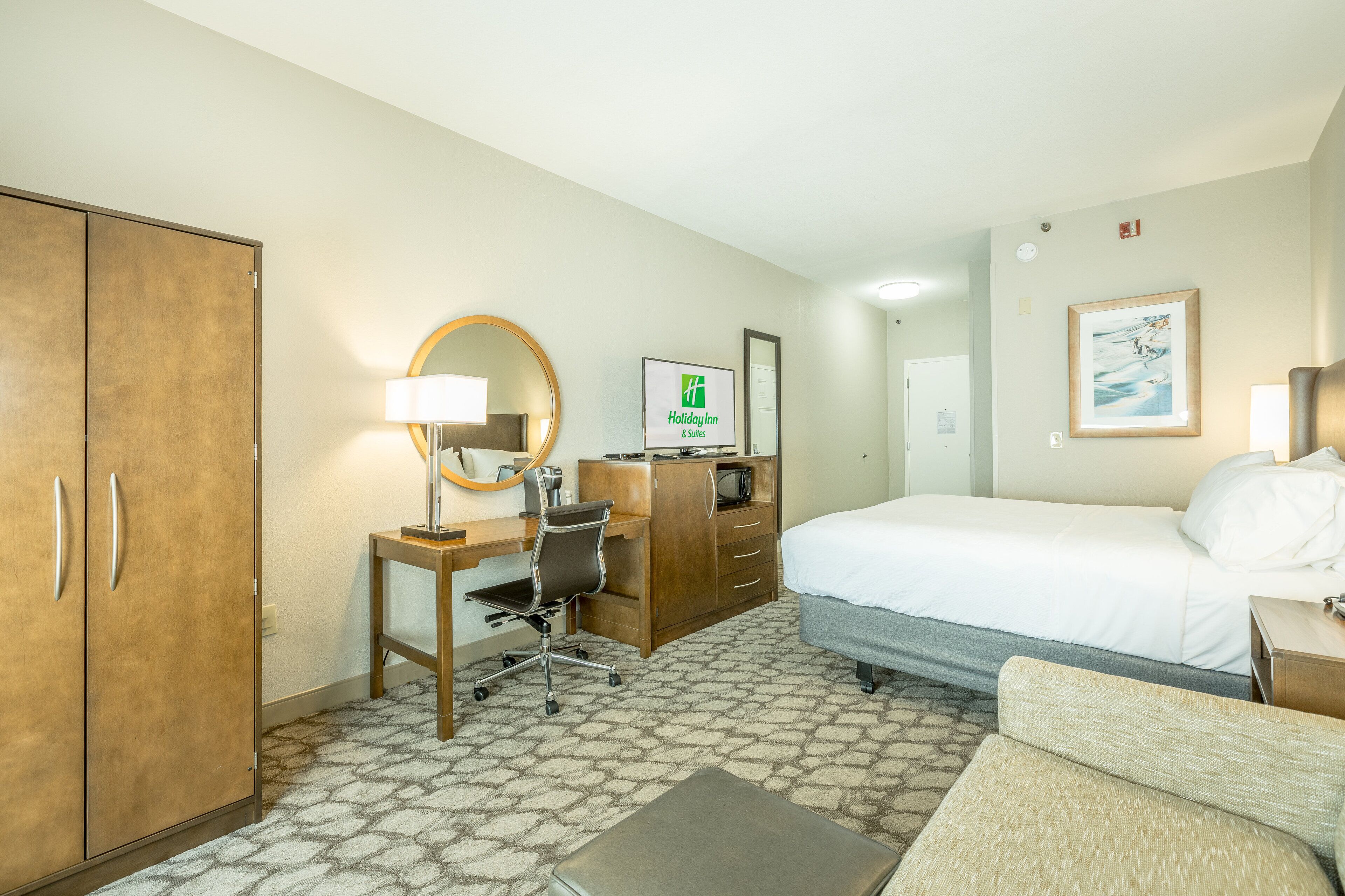 Une chambre d’hôtel comprenant un lit, un bureau, une chaise, une armoire et un tableau encadré au mur.