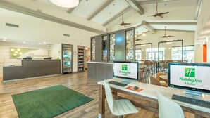 Un espace d’accueil d’un hôtel Holiday Inn, avec un plancher en bois, une moquette verte et un comptoir de réception équipé d’ordinateurs.
