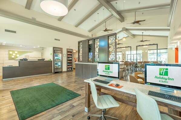 Un espace d’accueil d’un hôtel Holiday Inn, avec un plancher en bois, une moquette verte et un comptoir de réception équipé d’ordinateurs.