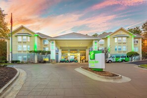 Een Holiday Inn & Suites met een overdekte ingang, een vlag en een groen-witte bestelwagen die ervoor geparkeerd staat.