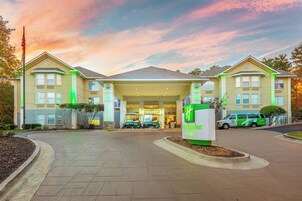 Un Holiday Inn & Suites con entrada cubierta, una bandera y una camioneta verde y blanca estacionada al frente.