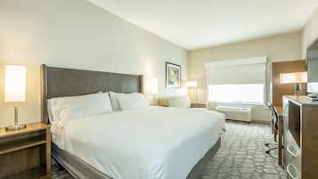Ein Hotelzimmer mit einem großen Bett, Nachttischlampen, einem Schreibtisch, einer Kommode und einem Fenster mit Jalousien.