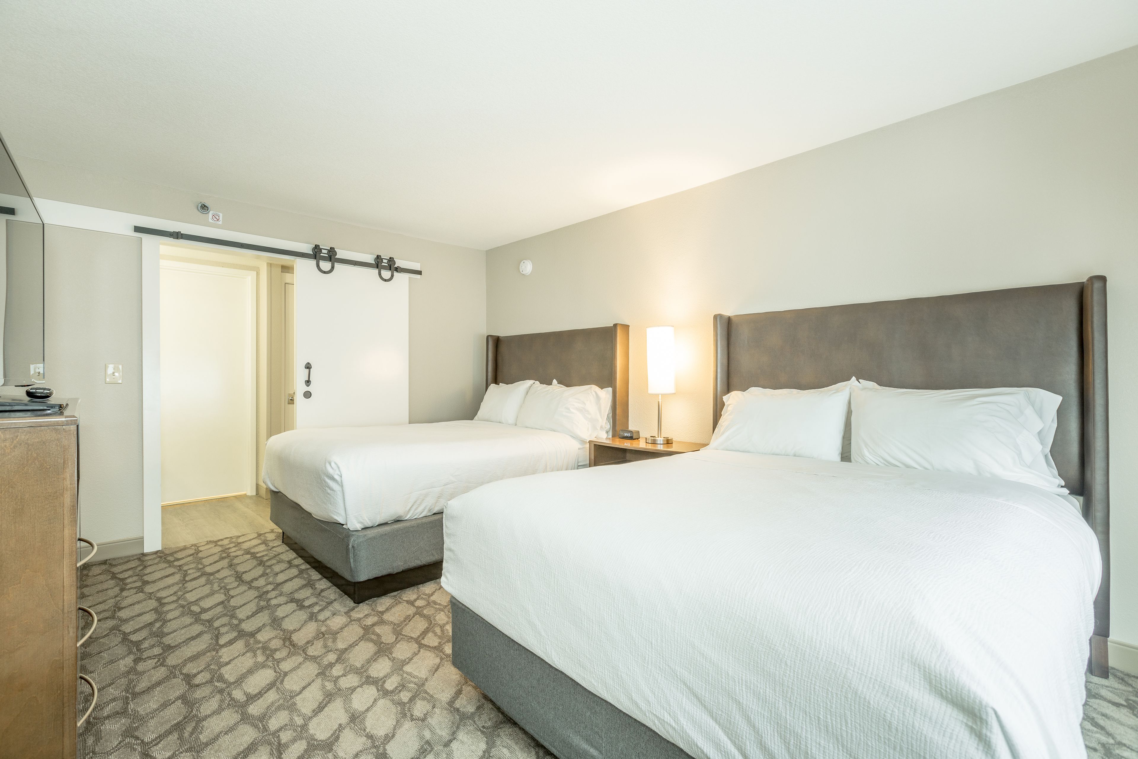 A hotel room with two beds, a desk, and a door.