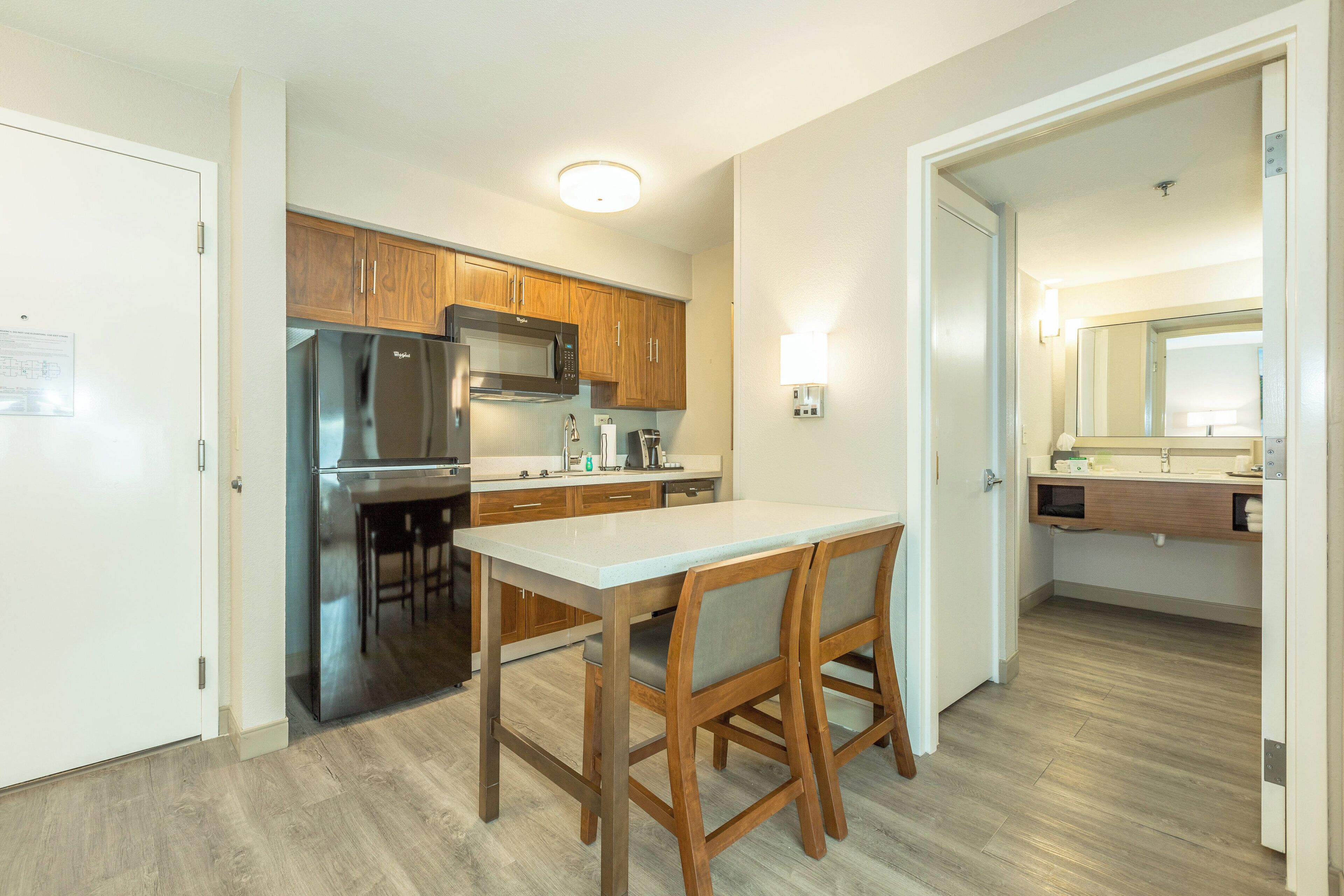 A compact kitchen with wooden cabinets, a stainless steel refrigerator, a microwave, and a dining area with a table and chairs.