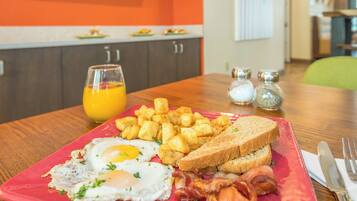 A breakfast plate with eggs, bacon, toast, and hash browns on a red plate.