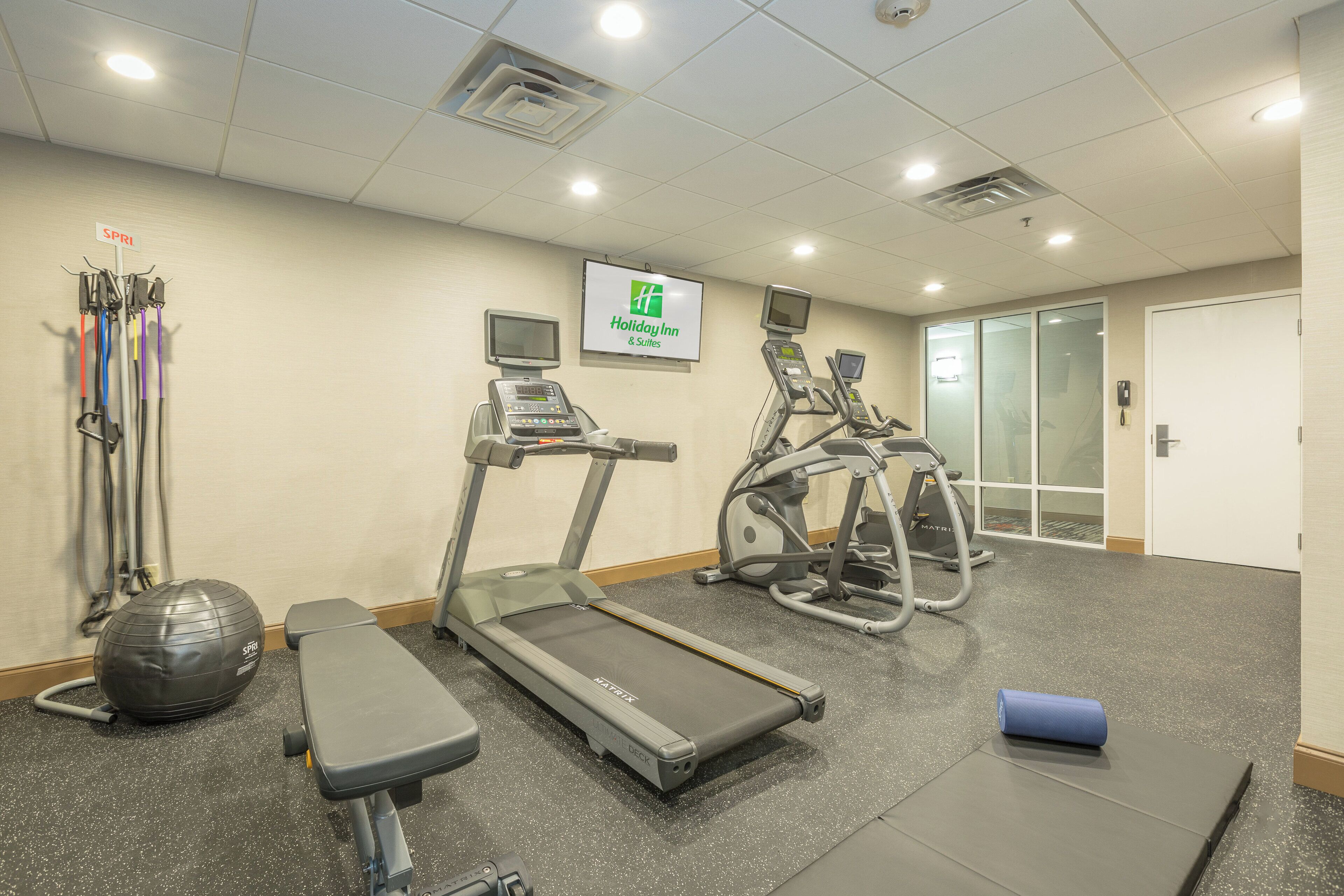 Et fitnesscenter med løbebånd, crosstrainere, en bænk og en motionscykel.