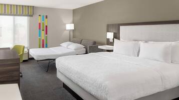 A hotel room with a large bed, a smaller bed, a desk, a chair, and a window with blinds.