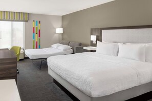 Habitación de hotel con una cama grande, una cama más pequeña, un escritorio, una silla y una ventana con persianas.