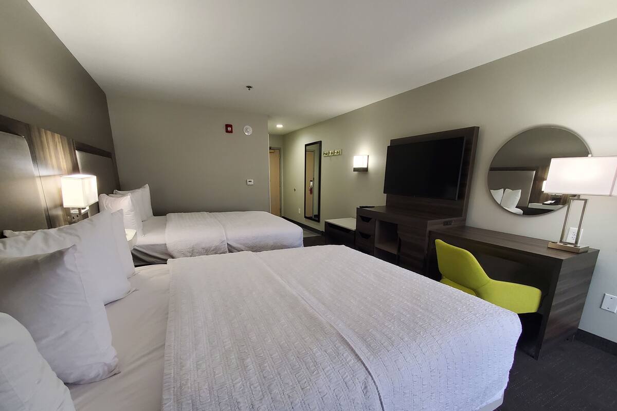 Quarto de hotel com duas camas, uma escrivaninha, uma cadeira, uma televisão e um espelho.