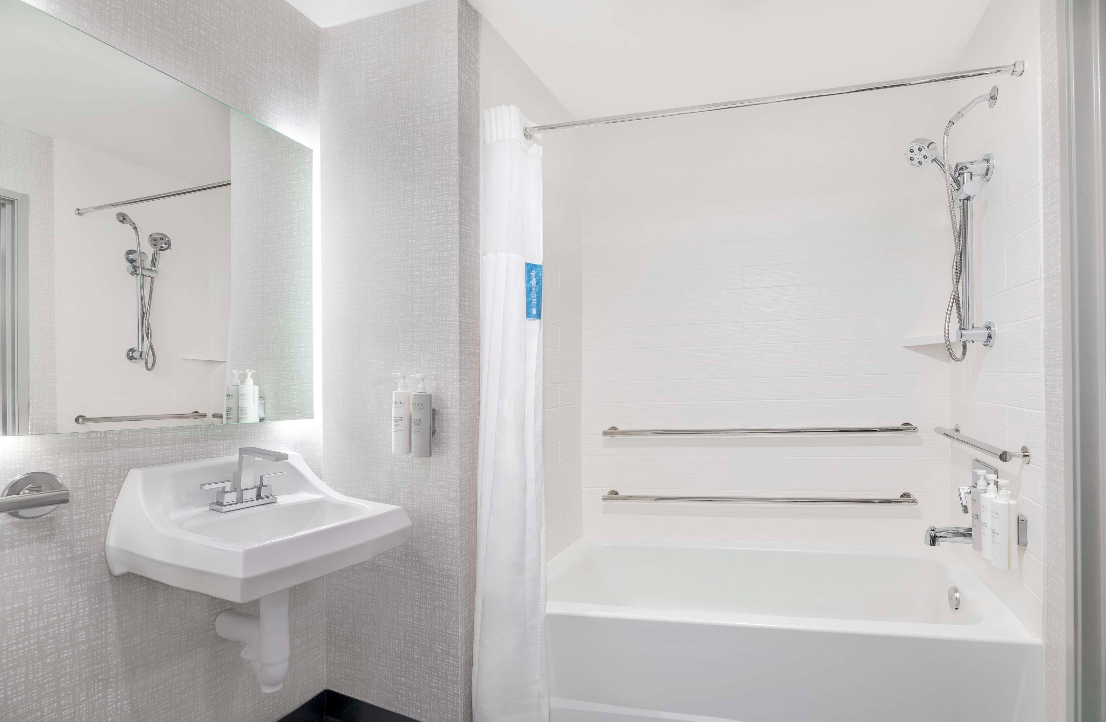 A modern bathroom with a white sink, mirror, and bathtub.