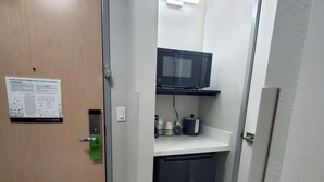 Un pasillo estrecho con una puerta a la izquierda, un microondas en un estante superior y una pequeña zona de kitchenette.