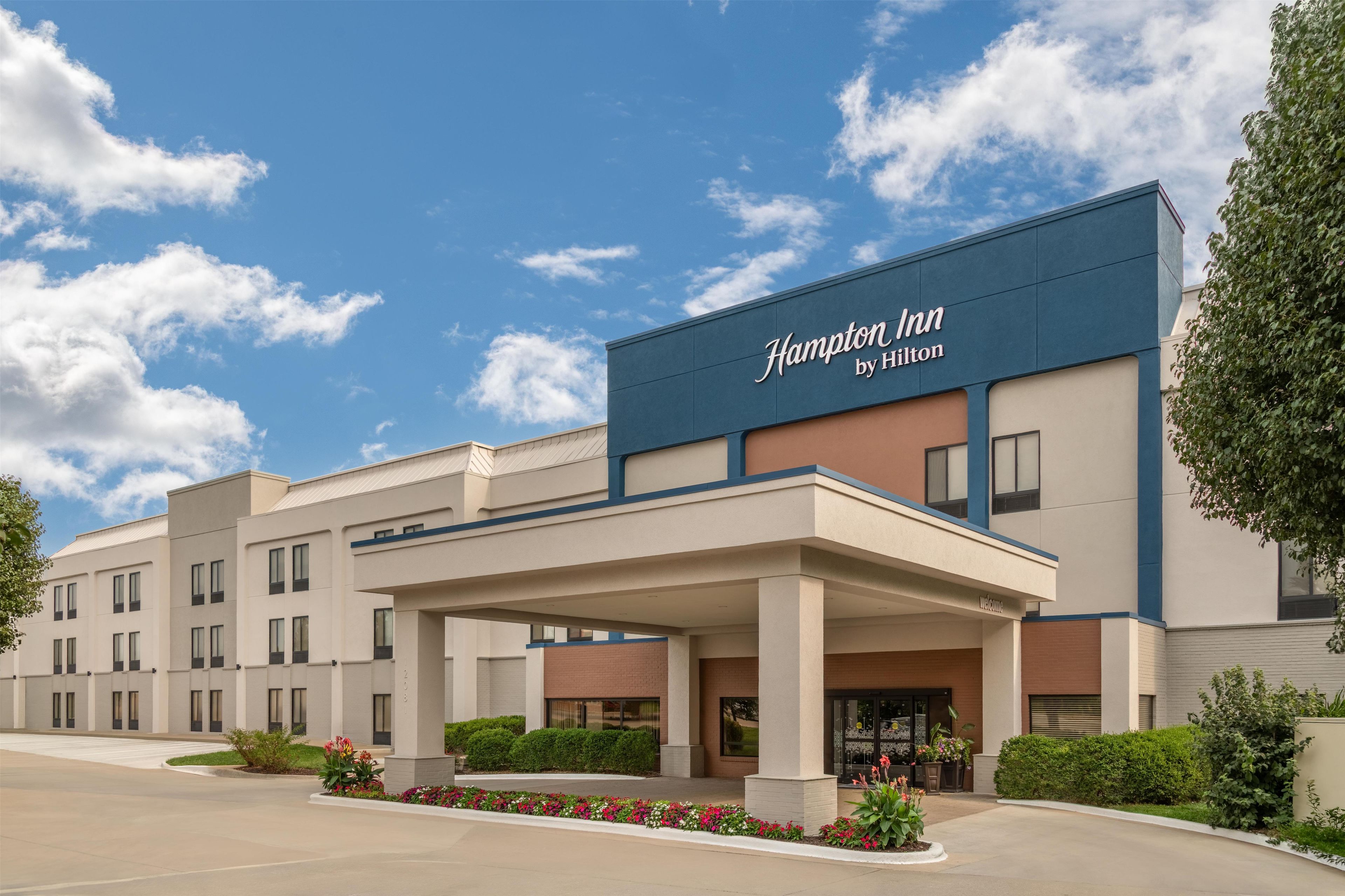 Un hotel Hampton Inn by Hilton con fachada moderna, un acceso cubierto y jardines ajardinados.