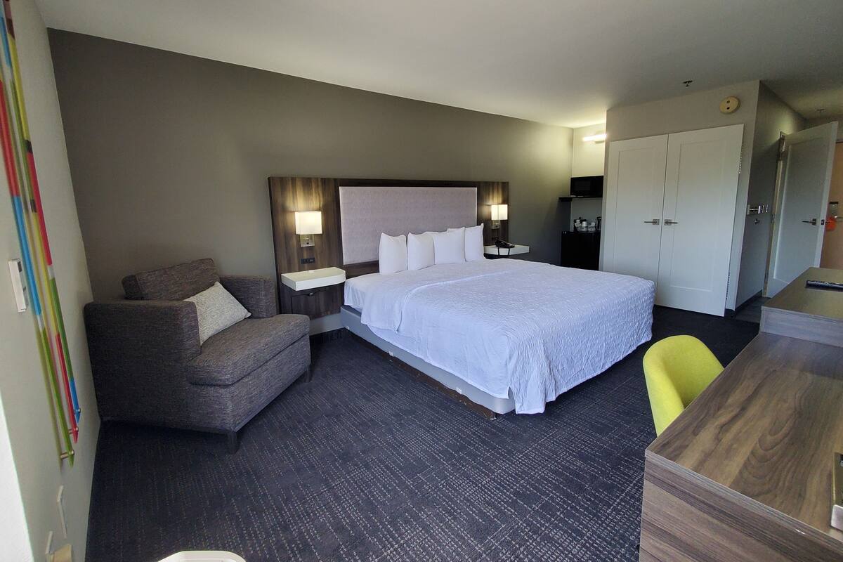 Quarto de hotel com uma cama grande, uma escrivaninha, uma cadeira e um pequeno sofá.