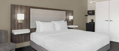 A hotel room with a large bed, two bedside tables with lamps, a wardrobe, and a microwave.
