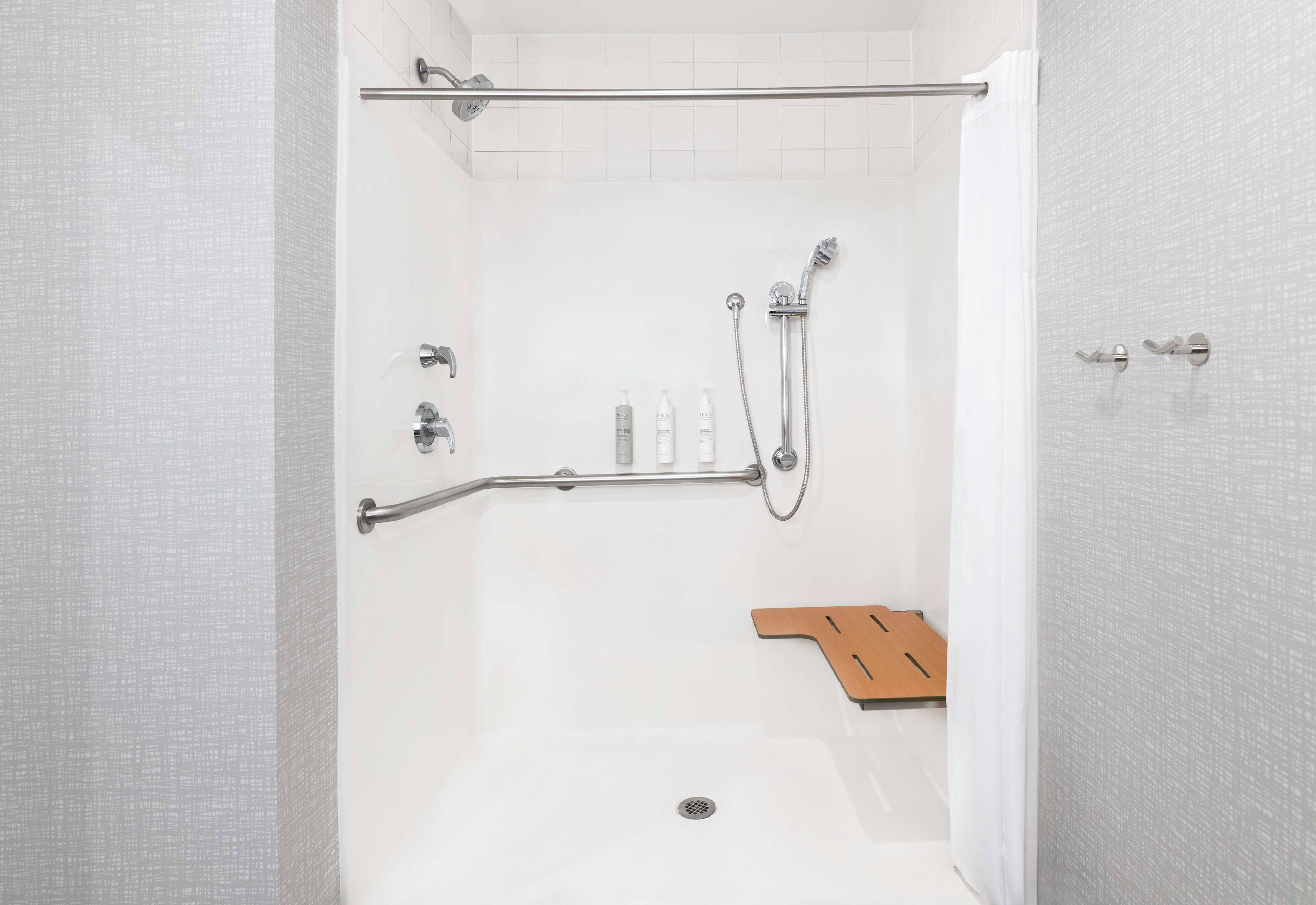 Zona de ducha con puerta de cristal, ducha, manecilla de ducha, toallero y estante de madera.