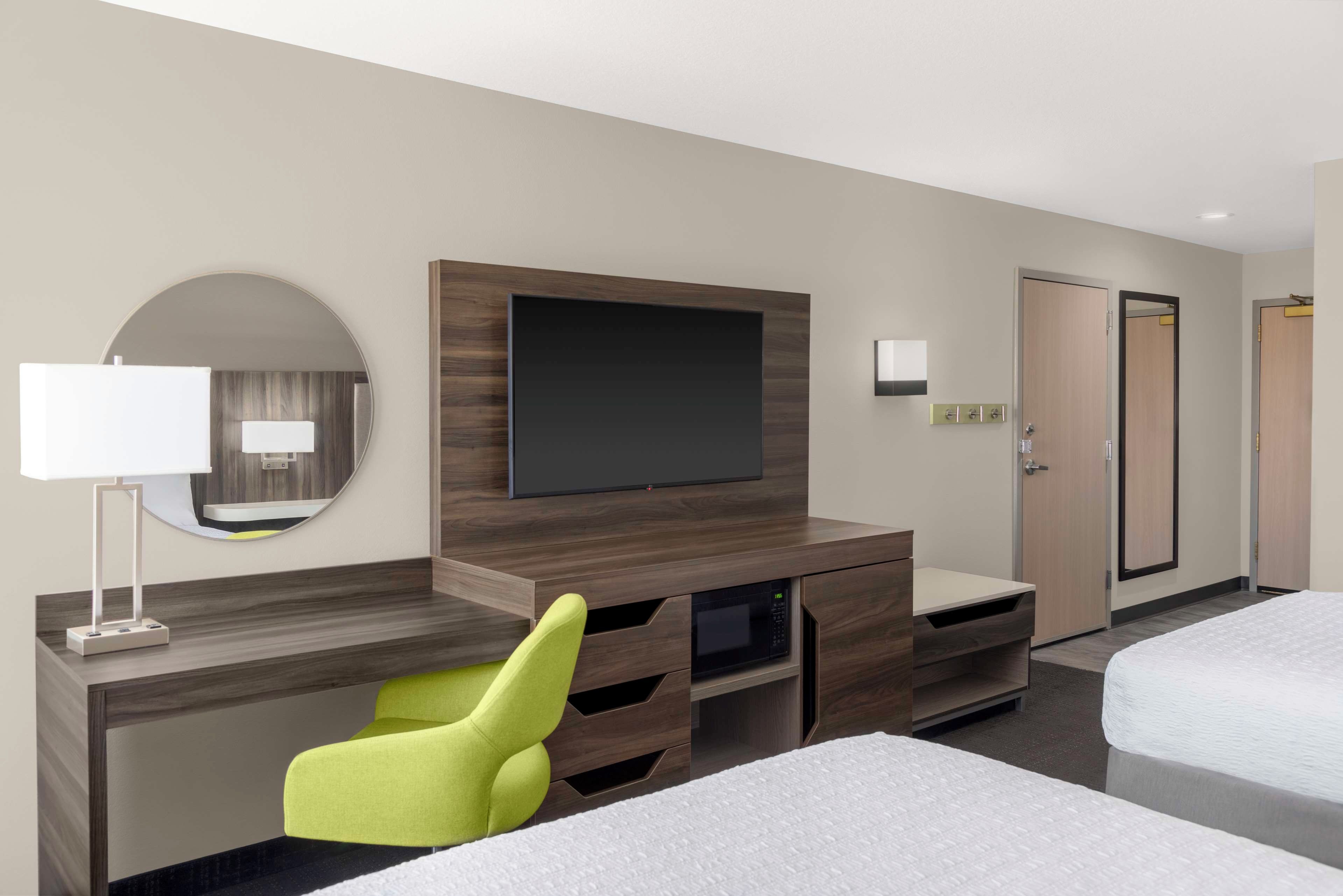 Una habitación de hotel con una cama, un escritorio con silla, un televisor, un espejo y un armario.
