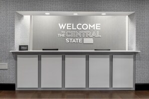 Una recepción con un cartel que dice 'WELCOME TO THE CENTRAL STATE', una placa de 'Hilton Honors' y un diseño limpio y moderno.