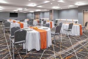 A conference room with multiple tables, each with a white tablecloth and orange runners, arranged in rows with grey chairs. - Hampton Inn Olathe (Olathe)
