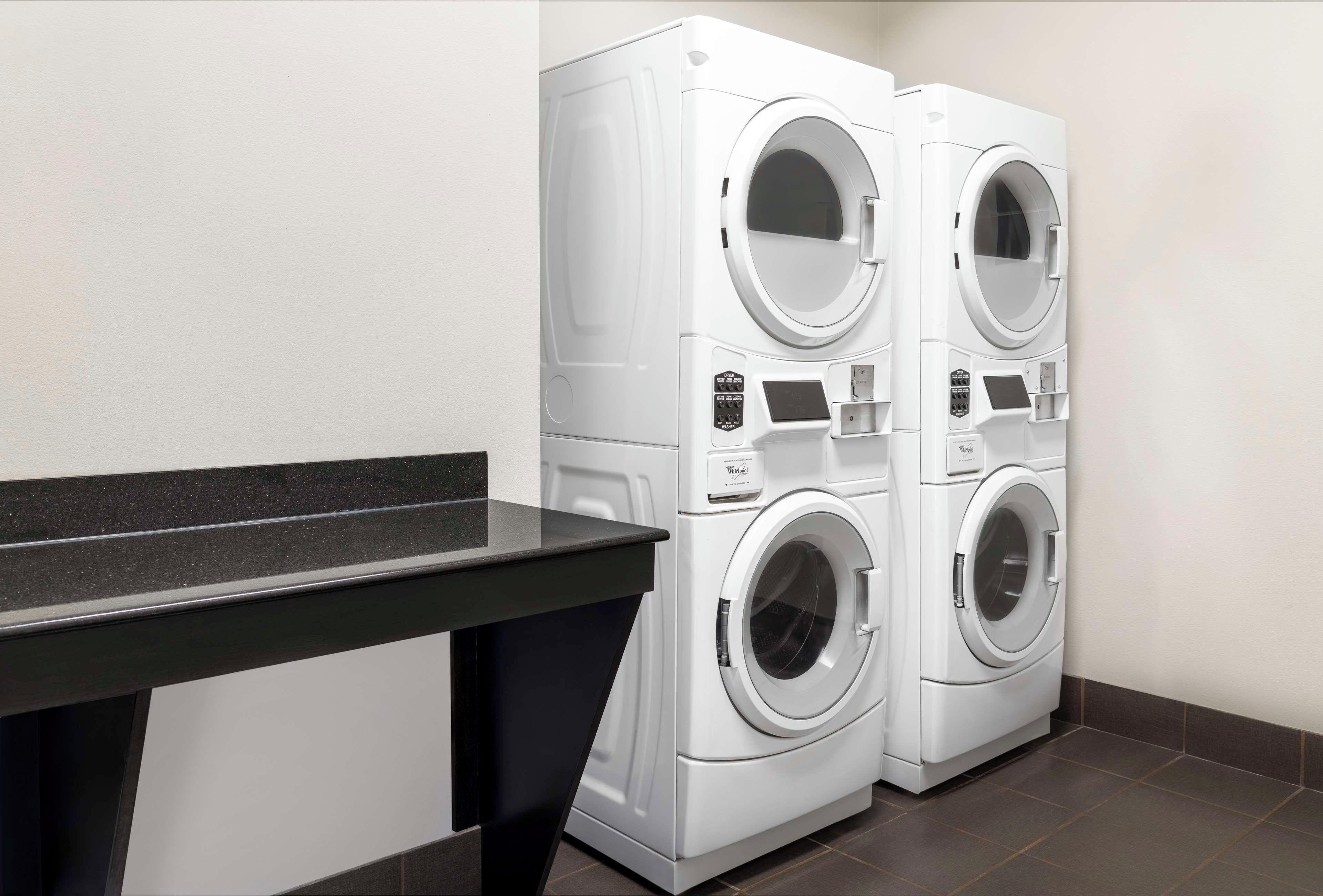 A laundry room with two stacked front-loading washing machines and a bench.