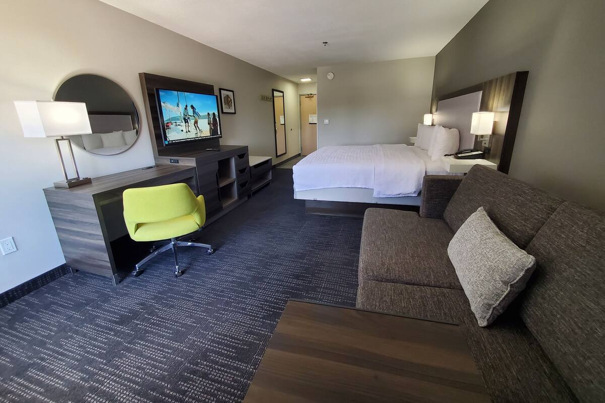 Quarto de hotel com cama, sofá, escrivaninha com televisão e uma cadeira.