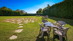 An outdoor seating area with a circular pattern of stepping stones on the grass, surrounded by a hedge and a clear blue sky. - Charlevoix Inn & Suites SureStay Collection by Best Western (Charlevoix)