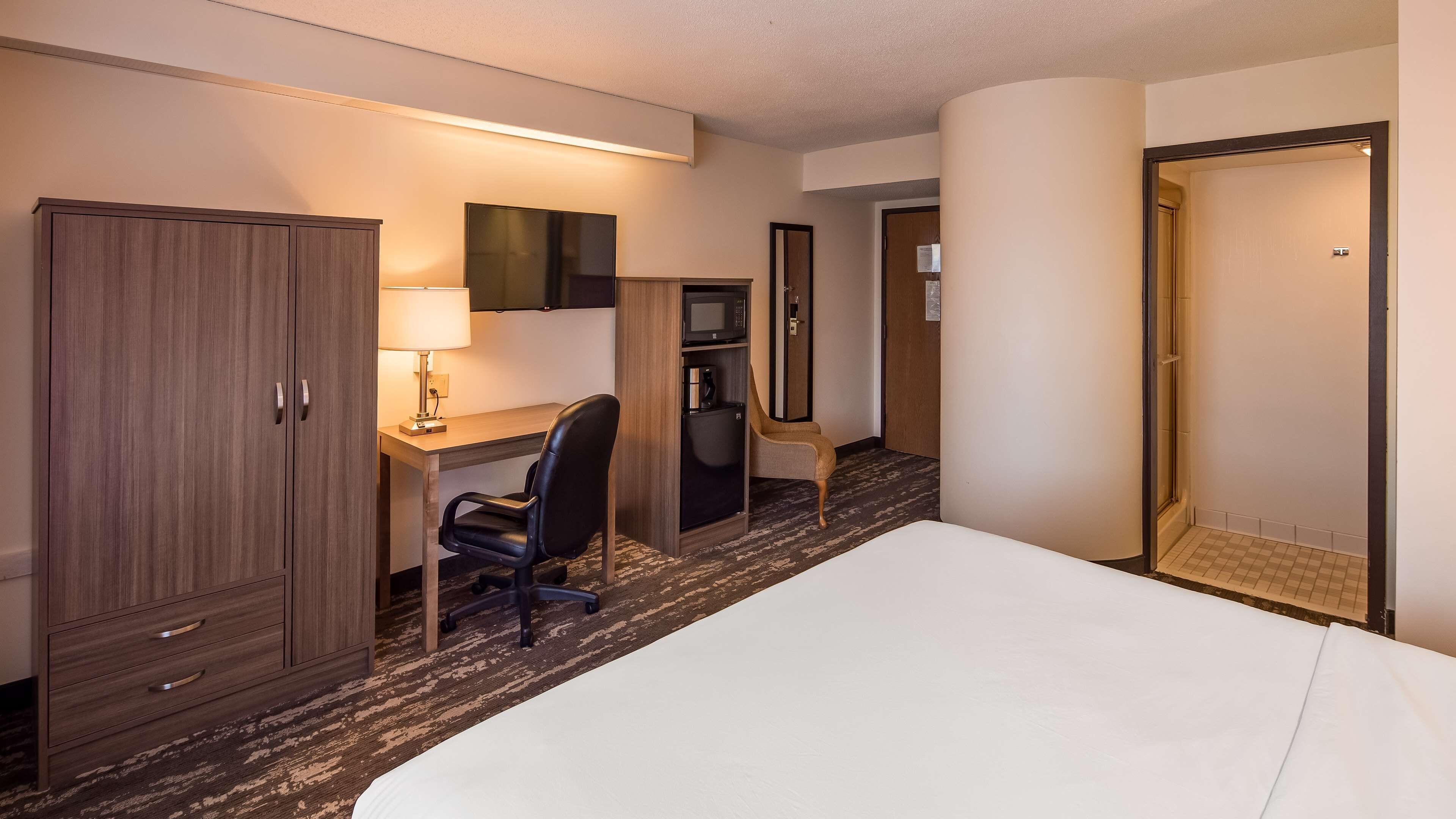 A hotel room with a bed, a desk with a lamp, a microwave, a refrigerator, and a wardrobe.