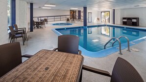 An indoor swimming pool with a lounge area, chairs, and a staircase leading to an upper level. - Charlevoix Inn & Suites SureStay Collection by Best Western (Charlevoix)