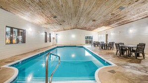 An indoor swimming pool with a wooden ceiling, tiled floor, and a seating area with tables and chairs. - Americas Best Value Inn Marquette (Marquette)