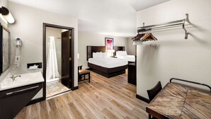 A hotel room with a wooden floor, a large bed, a bedside table, a mirror, a shower area, and a coat rack. - Americas Best Value Inn Marquette (Marquette)