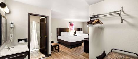 Une chambre d’hôtel avec un plancher en bois, un grand lit, une table de chevet, un miroir, un espace douche et un porte-manteau.