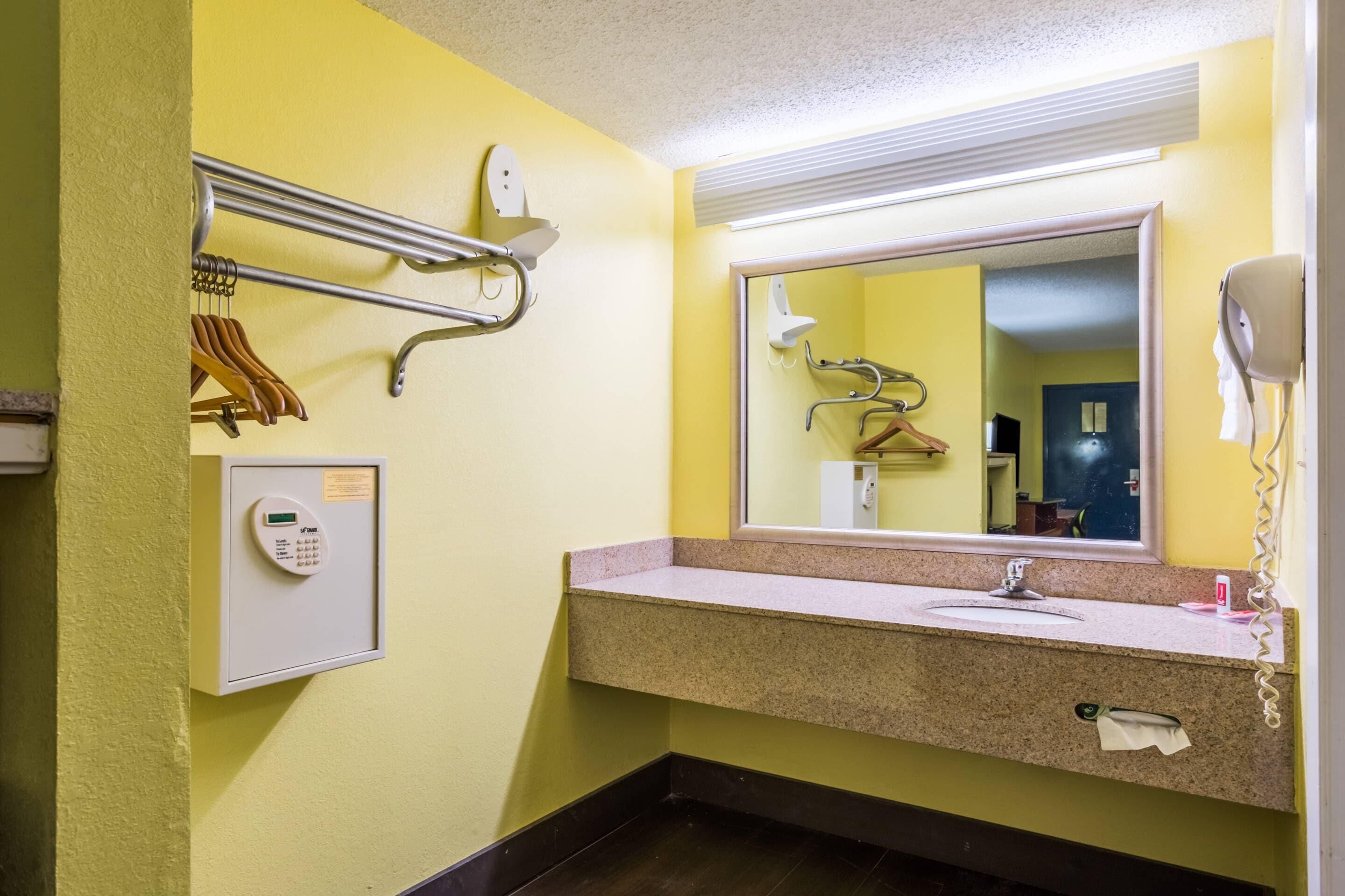 A bathroom with a yellow wall, a sink with a mirror, a towel rack, a hairdryer, and a control panel.