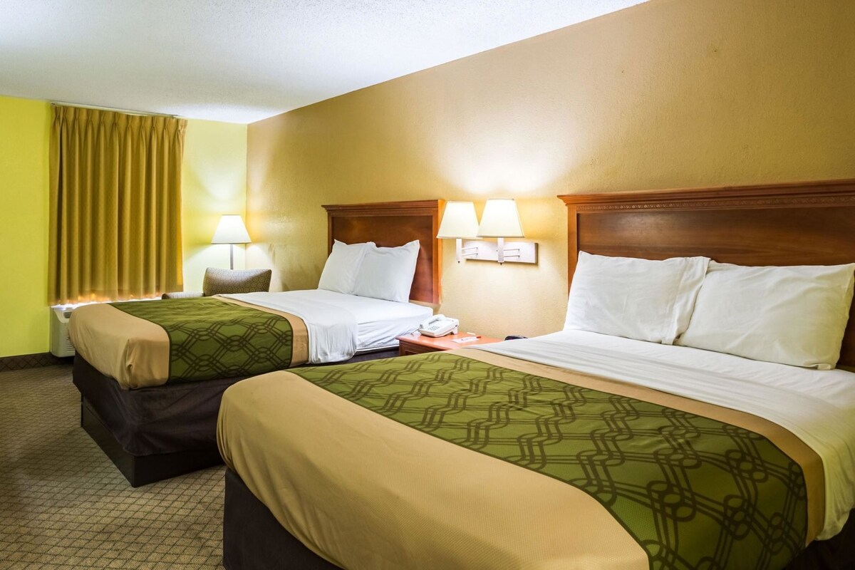 A hotel room with two beds, each with a headboard, bedside lamps, and a telephone on the nightstand.