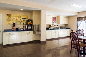 Una cocina de hotel con estación de café, un reloj y un comedor con sillas y una mesa.