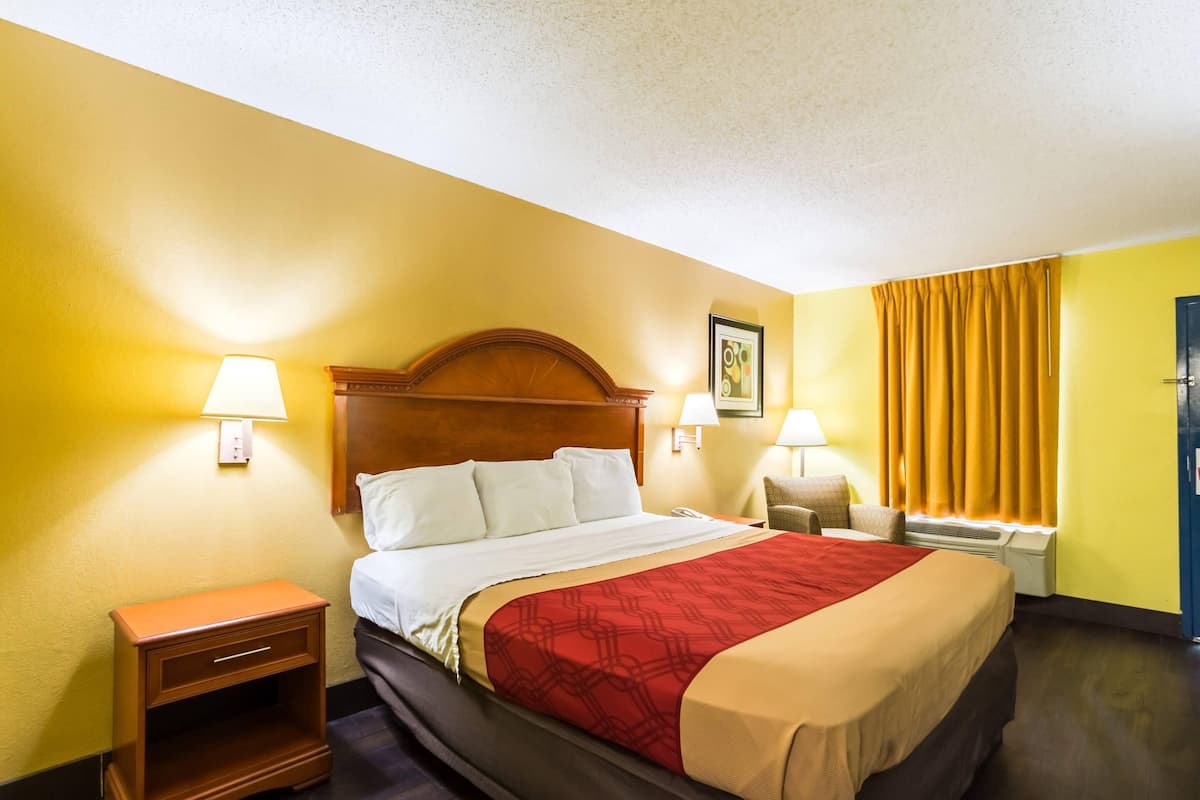 Una habitación de hotel con cama, mesita de noche, lámpara y ventana con cortinas.