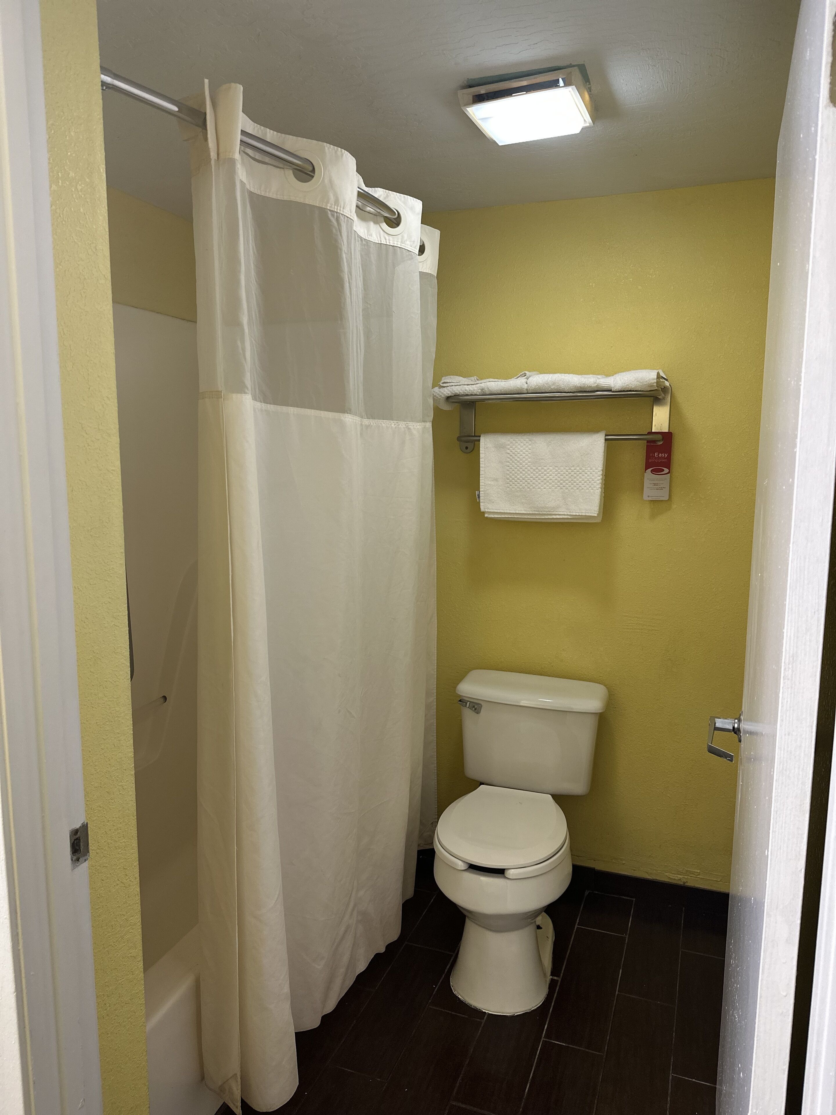 Un baño con inodoro blanco, cortina de ducha y toallero con una toalla blanca.