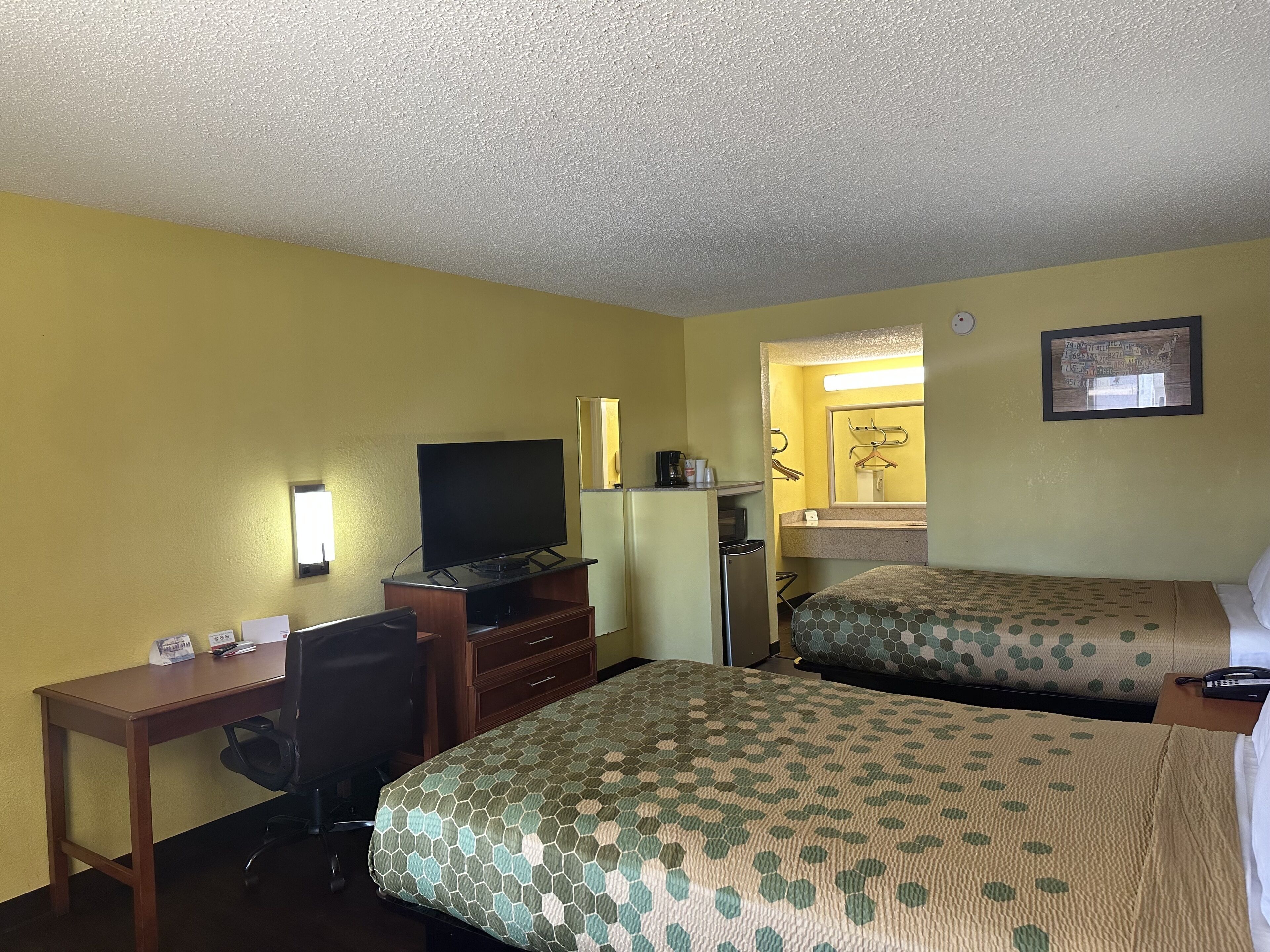 A hotel room with two beds, a desk, a television, a dresser, and a bathroom visible through an open door.