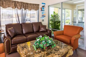 A brown leather sofa, an orange armchair, and a marble coffee table with a floral centerpiece in a room with large windows and a view of the outdoors. - Econo Lodge Picayune (Picayune)