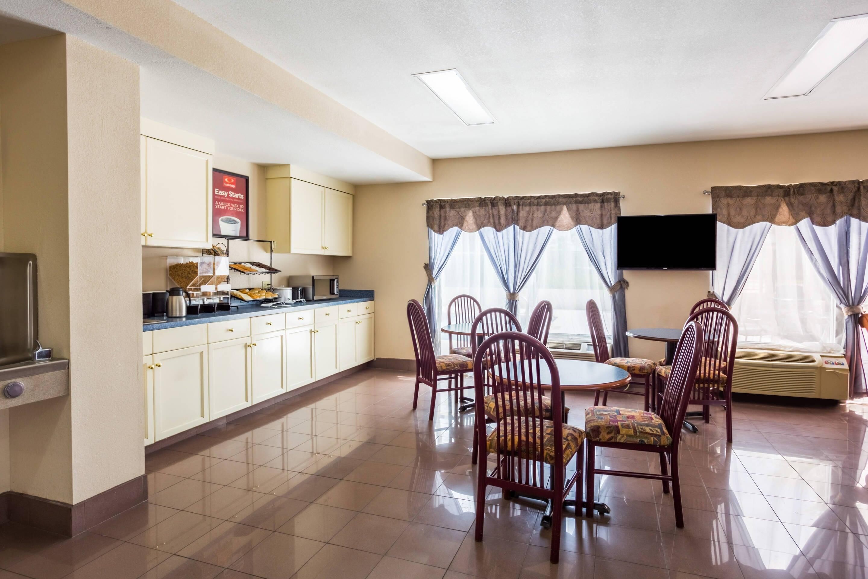 Habitación de hotel con comedor, kitchenette, televisión de pantalla plana y ventanas grandes con cortinas.