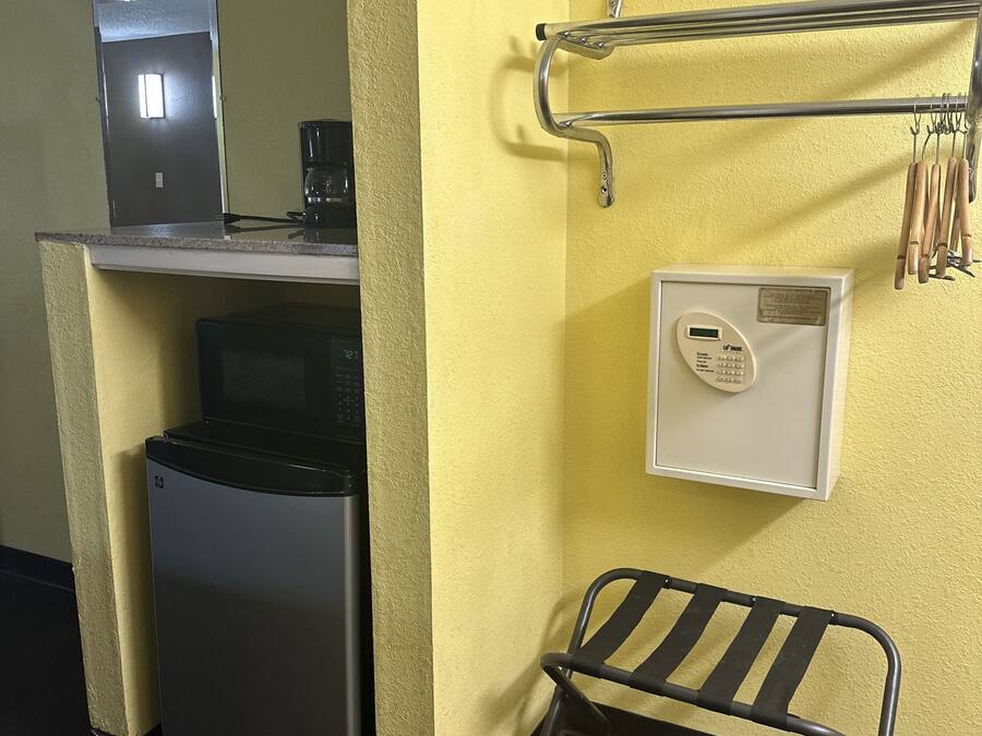 A compact kitchenette with a coffee maker, a small refrigerator, a microwave, and a built-in oven. There is a metal rack with utensils and a small bench.