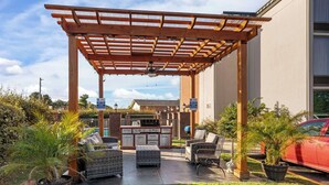 Un patio al aire libre con pérgola, zona de estar, parrilla y plantas en macetas.