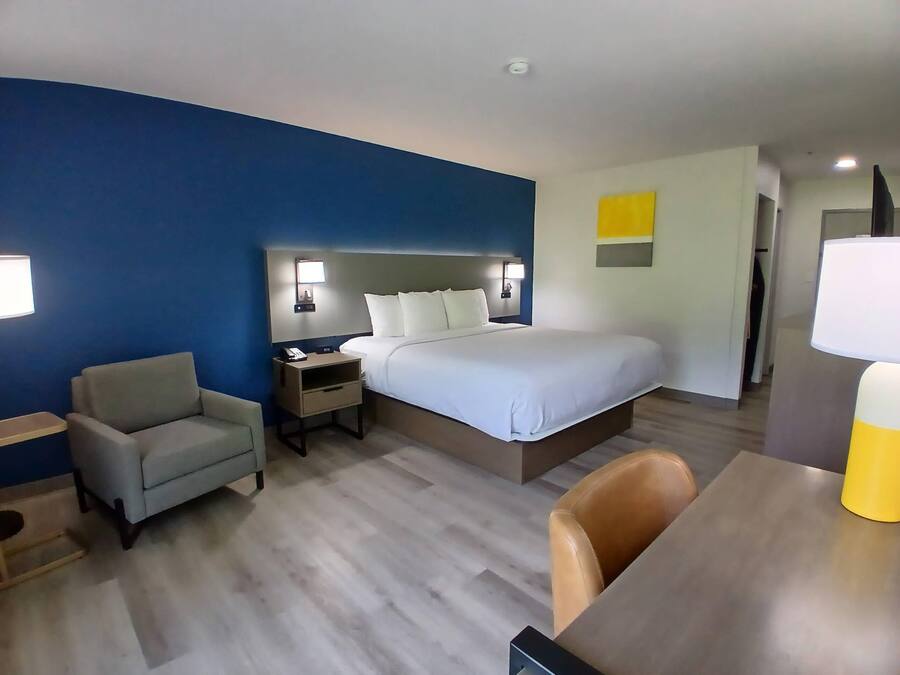 A hotel room with a bed, bedside tables, a chair, a desk, and a lamp.