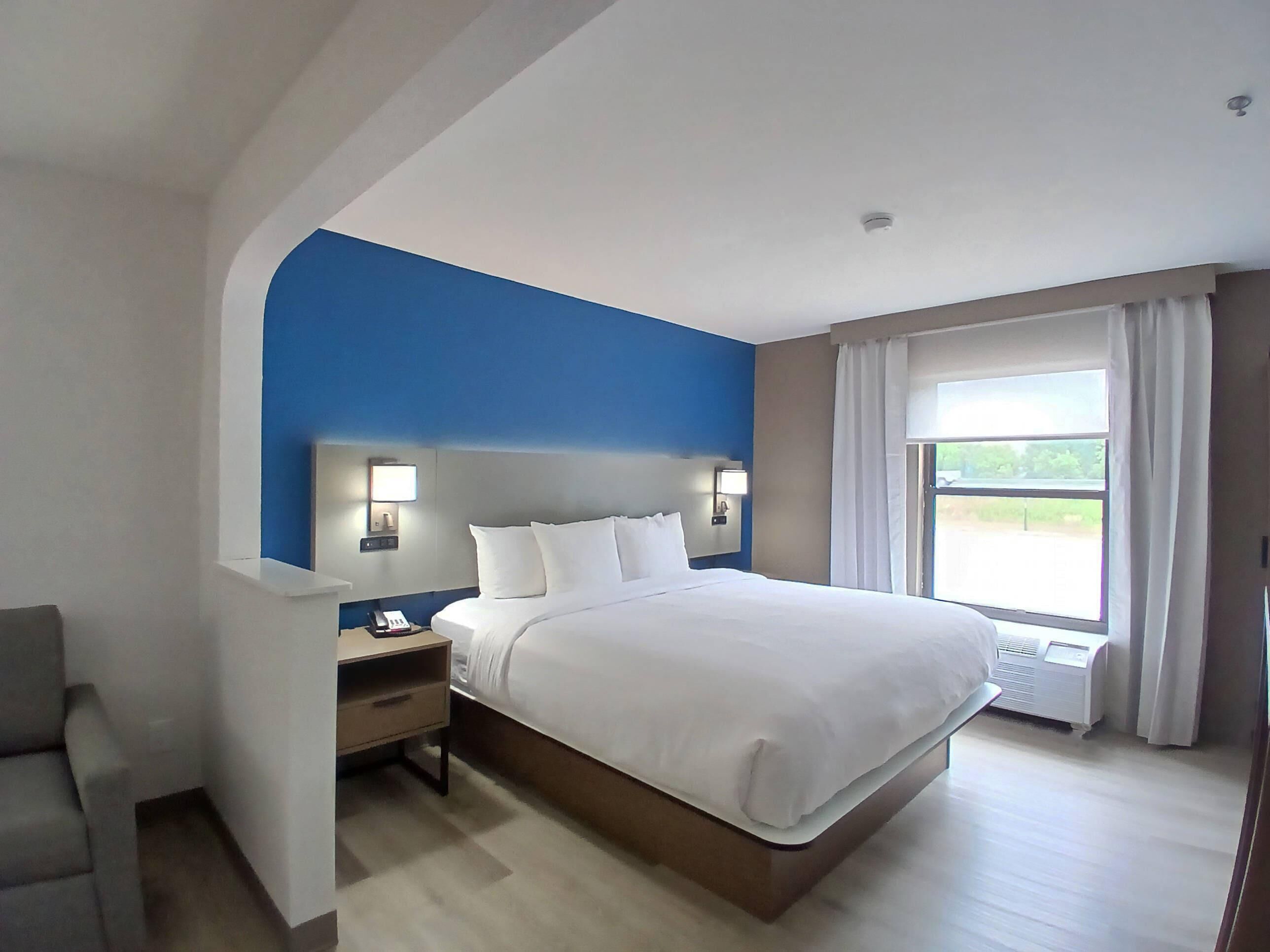 Habitación de hotel con una cama grande, mesitas de noche, un escritorio y una ventana con cortinas.